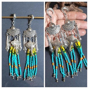 Puede incluir: Un par de pendientes colgantes de plata con un dije de elefante y cuentas turquesa y amarillas.