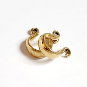 May include: A pair of gold-toned hoop earrings with a unique, twisted design. The earrings are made of metal and have a smooth, polished finish.