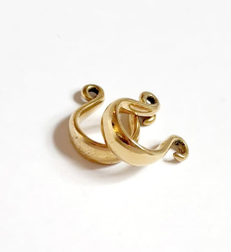 May include: A pair of gold-toned hoop earrings with a unique, twisted design. The earrings are made of metal and have a smooth, polished finish.