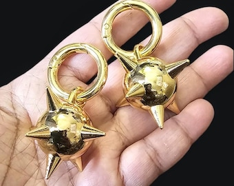 May include: Two gold-colored spiked ball keychains with a ring attachment. The keychains are held in a hand.