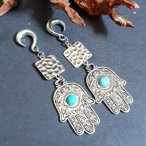 Puede incluir: Un par de pendientes de plata con una piedra turquesa en el centro de cada pendiente. Los pendientes tienen forma de mano con un ojo en la palma. Los pendientes cuelgan de un gancho de plata.