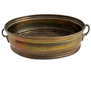 Może przedstawiać: Owalna mosiężna miska w stylu antycznym z dwoma małymi uchwytami. Miska ma szeroki brzeg i lekko iridiscentne wykończenie, z nutami złota, zieleni i brązu. Prawdopodobnie służy do celów dekoracyjnych.