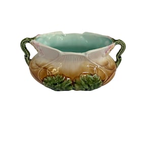 Peut inclure: Un bol en céramique à deux anses, doté d'un intérieur bleu clair et d'une base extérieure brune. L'extérieur est orné de motifs de feuilles vertes en relief à la base et d'accents floraux roses près du bord supérieur, avec un fini brillant.