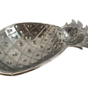 Könnte beinhalten: Silberne Ananas-Servierplatte mit strukturierter Oberfläche und einem erhöhten, detaillierten Ananas-Oberteil.