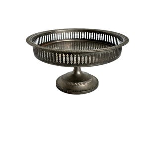 May include: A silver-toned, pedestal serving tray with a round, pierced rim and a decorative, fluted base. The tray is elevated on a short, rounded pedestal. The metal has a slightly aged appearance.