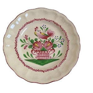 Pode incluir: Um prato de cerâmica branco com um galo rosa e um desenho floral. O prato tem uma borda ondulada e uma borda rosa e branca.