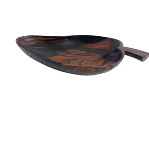 Op de afbeelding: Een donkerbruine houten serveerschaal in de vorm van een blad met een handvat. De schaal heeft een natuurlijk houtnerfpatroon.