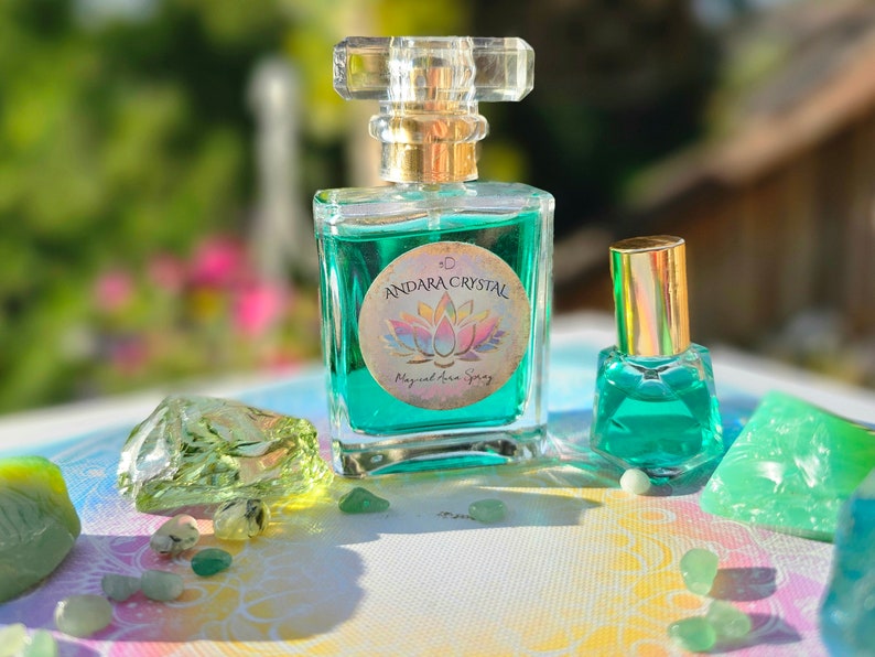 Puede incluir: Dos botellas de vidrio de l&iacute;quido verde con tapas doradas y etiquetas que dicen "Andara Crystal Magical Aura Spray". Las botellas est&aacute;n sobre una superficie blanca con cristales verdes.