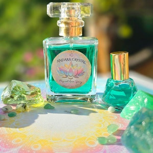 Puede incluir: Dos botellas de l&iacute;quido verde con tapas y etiquetas doradas. La botella m&aacute;s grande tiene una etiqueta que dice "Andara Crystal Magical Aura Spray". Las botellas est&aacute;n rodeadas de cristales verdes.