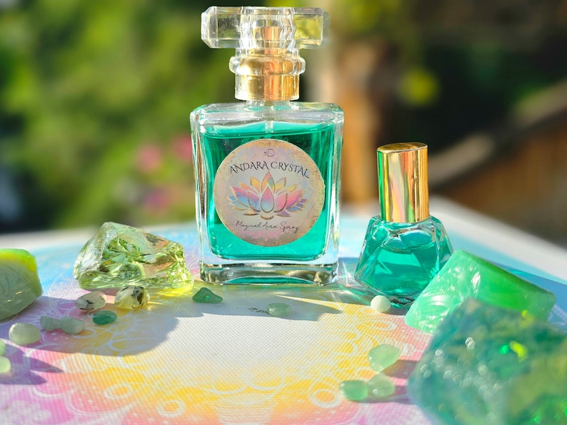 Puede incluir: Dos botellas de l&iacute;quido verde con tapas y etiquetas doradas. La botella m&aacute;s grande tiene una etiqueta que dice "Andara Crystal Magical Aura Spray". Las botellas est&aacute;n rodeadas de cristales verdes.