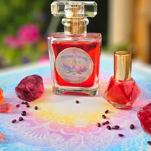 May include: Two glass bottles of red liquid with gold caps. The larger bottle has a label that reads "Andara Crystal Magical Aura Spray". The bottles are surrounded by red crystals on a colorful mandala background.