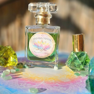 May include: A clear glass bottle with a gold cap and a green liquid inside. The bottle has a label that says "Andara Crystal Magical Aura Spray". The bottle is sitting on a table with a rainbow pattern and surrounded by green and blue stones.