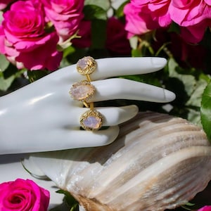 Può includere: Tre anelli d'oro con pietre ovali di opale bianco incastonate in un design floreale. Gli anelli sono esposti su una mano di manichino bianca.