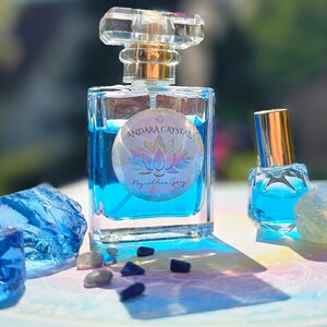 May include: Two blue glass bottles of essential oil with gold caps and labels. The larger bottle has a label that reads "Andara Crystal Magical Aura Spray". The bottles are surrounded by blue and clear crystals.