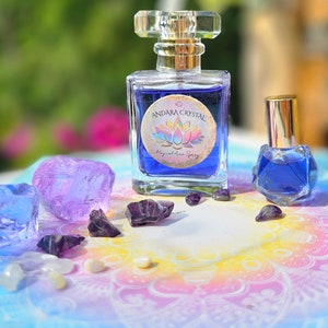 May include: Two bottles of blue essential oil with a label that says "Andara Crystal Magical Aura Spray". The bottles are surrounded by purple and blue crystals on a colorful background.
