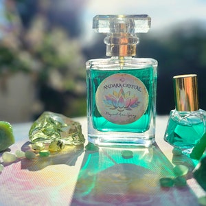 Puede incluir: Dos botellas de l&iacute;quido verde con tapas doradas. La botella m&aacute;s grande tiene una etiqueta que dice "Andara Crystal Magical Aura Spray". Las botellas est&aacute;n sobre una superficie blanca con piedras verdes.