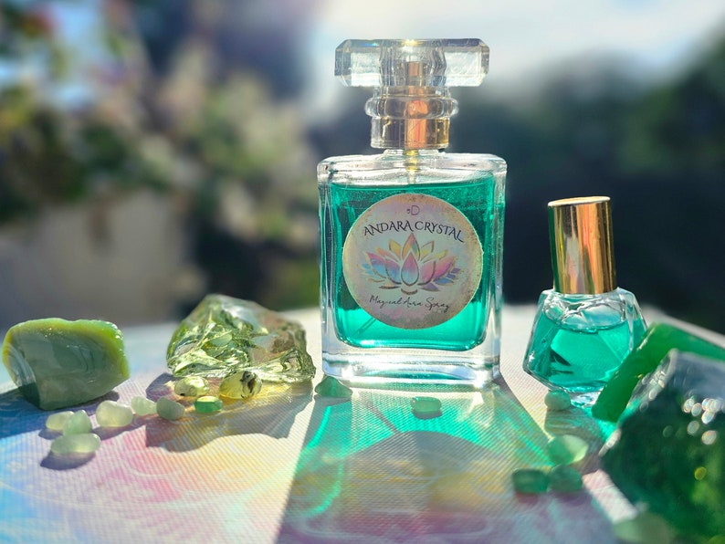 Puede incluir: Dos botellas de l&iacute;quido verde con tapas doradas. La botella m&aacute;s grande tiene una etiqueta que dice "Andara Crystal Magical Aura Spray". Las botellas est&aacute;n sobre una superficie blanca con piedras verdes.