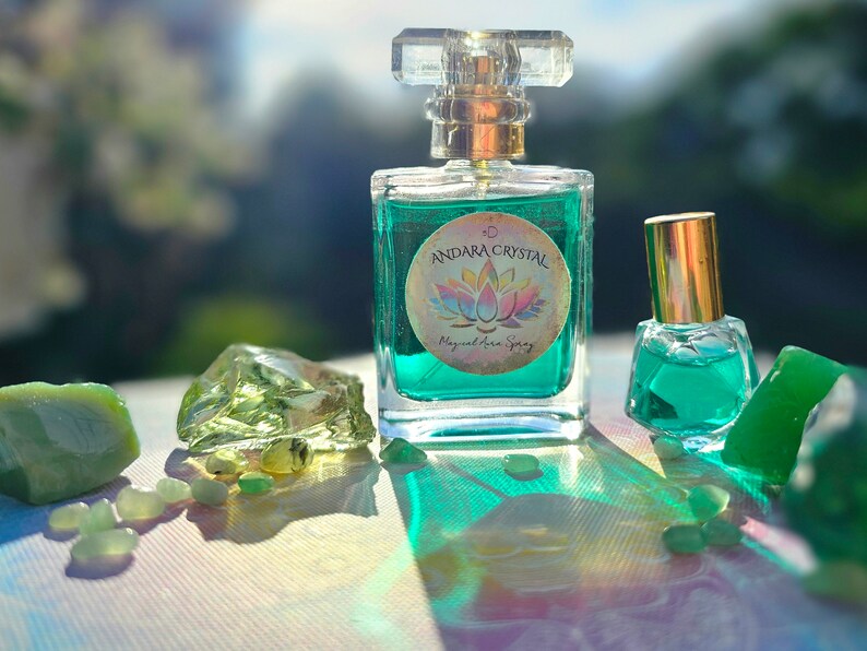 Puede incluir: Dos botellas de l&iacute;quido verde con tapas doradas y etiquetas. La botella m&aacute;s grande tiene una etiqueta que dice "Andara Crystal Magical Aura Spray". Las botellas est&aacute;n rodeadas de piedras verdes.