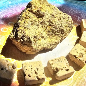 May include: A large, rough-textured, yellow-brown rock with several smaller, cube-shaped stones. The cubes have a similar colour and texture, with some showing holes. The objects are arranged on a colourful, patterned surface.