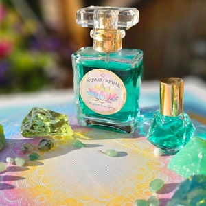 Puede incluir: Una botella de vidrio transparente con una tapa dorada y un l&iacute;quido verde en su interior. La botella tiene una etiqueta que dice "Andara Crystal Magical Aura Spray". La botella est&aacute; rodeada de cristales y piedras verdes.