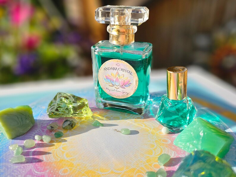 Puede incluir: Una botella de vidrio transparente con una tapa dorada y un l&iacute;quido verde en su interior. La botella tiene una etiqueta que dice "Andara Crystal Magical Aura Spray". La botella est&aacute; rodeada de cristales y piedras verdes.