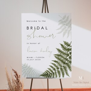 May include: A white sign with green ferns on it, announcing a bridal shower for Lauren Henley in Miami, Florida on July 13, 2020. The sign is on an easel.
