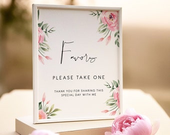 May include: A white frame with a sign that says "Favors Please Take One Thank You for Sharing This Special Day With Me". The sign is decorated with pink and green watercolour flowers. The sign is sitting on a light brown surface with pink flowers.