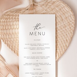 May include: A white wedding menu card with a minimalist design. The text "The Menu" is written in a script font at the top of the card. The menu items are listed in a simple, clean font. The date "30.11.2021" and the names "Heather and James" are at the bottom of the card.