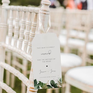 May include: A white wooden chair with a tag attached to it. The tag says "This seat is kindly reserved for the mother of the bride." The tag also includes the names "Joanna & James" and the date "13.10.2023".