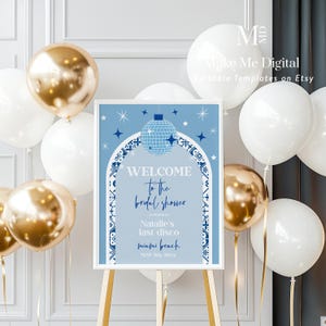 May include: Blue and white welcome sign with a disco ball graphic for a bridal shower. The sign says "Welcome to the bridal shower in honor of Natalie's last disco, Sunrise Beach, May 9th, 20xx".