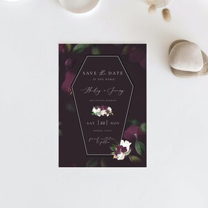 May include: A black and purple save the date card with a coffin-shaped frame. The text reads "Save the Date... If you dare!"  "Hilary & Jering are getting married"  "Sat 22 Nov"  "Boerne, Texas"  "Formal invitation to follow"