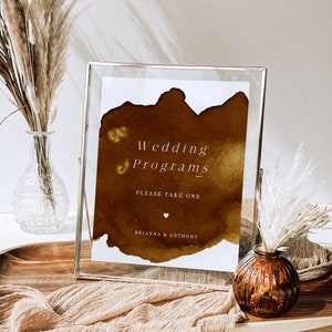 Może przedstawiać: Tablica w złotej ramie z brązowym akwarelowym tłem, na którym widnieje napis "Wedding Programs" wraz z tekstem "Please take one" i "Brianna & Anthony" w kolorze białym.