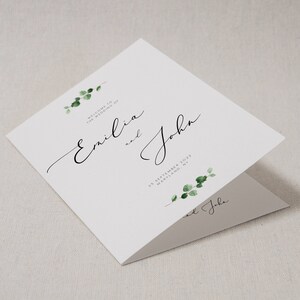 Puede incluir: Una invitación de boda blanca con ilustraciones de follaje verde. El texto dice "Bienvenido a la boda de Emilia y John, 25 de septiembre de 2022, Maryland, NY".