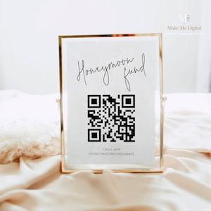 Puede incluir: Un cartel blanco con marco dorado, que presenta el texto "Honeymoon Fund" en escritura cursiva negra. Debajo del texto se muestra un código QR en blanco y negro, con las palabras "Cash App" y "HoneymoonFundName" impresas debajo del código.