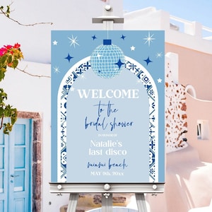 May include: A blue and white welcome sign with a disco ball and stars. The sign reads "Welcome to the bridal shower in honor of Natalie's last disco Miami Beach May 9th, 20xx".