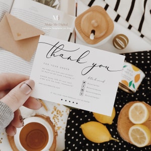 May include: A white thank you card with black text. The card says "Thank you" in a script font and includes the text "For your order" and "We hope you love your product as much as we loved creating it!" The card also includes social media icons and the text "Let's be social" and "If you love your product, let us know!" The card is sitting on a table with a cup of tea, lemons, and a wooden box.