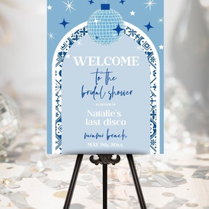 May include: Blue and white welcome sign for a bridal shower with a disco ball and stars. The text reads "Welcome to the bridal shower in honor of Natalie's last disco Miami Beach May 9th, 20xx".