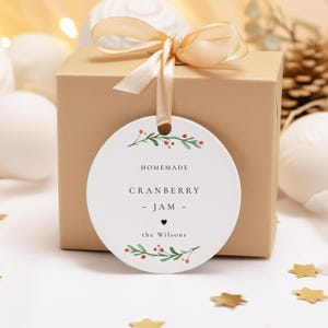 May include: A round white gift tag with a green leafy border and red berries. The tag says "Homemade Cranberry Jam - the Wilsons" with a small heart symbol.