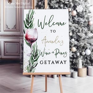 May include: A white sign on a wooden easel with the text "Welcome to Amanda's Wine + Pines Getaway." The sign features a watercolor illustration of a wine glass and greenery. The background includes a Christmas tree.