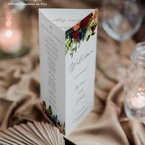 May include: A tri-fold wedding ceremony program with a floral design featuring red, pink, and blue flowers. The text on the program reads "The Wedding Party" and "Welcome to the Wedding of Melanie and Jay". The date and location of the wedding are also included.