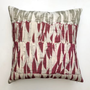 May include: A decorative throw pillow with a geometric pattern of white and burgundy leaves on a cream background.