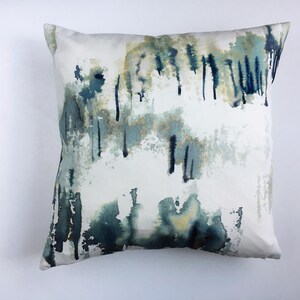 Op de afbeelding: Een wit kussen met een abstract ontwerp met blauwe, groene en gele aquarel-achtige vlekken en strepen.