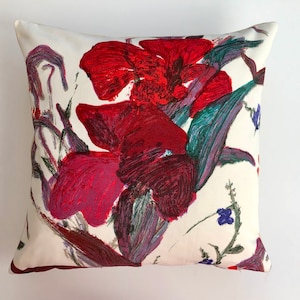 May include: A white cushion with a floral print featuring large red and purple flowers with green leaves.