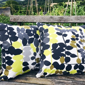 May include: Two decorative throw pillows with a white background and a pattern of black, yellow, and grey leaves. The pillows are sitting on a wooden bench.