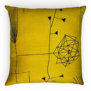 May include: Square yellow cushion featuring a black abstract geometric design. The design incorporates lines, triangles, and a central geometric shape. The cushion has a textured appearance and is likely made of fabric.