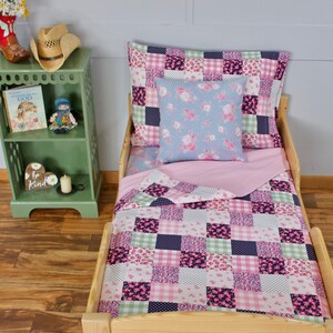 Puede incluir: Un juego de cama para cama de niño en patchwork rosa y azul con una almohada de estampado floral. La cama está hecha de madera natural y tiene una colcha rosa y blanca con un diseño de patchwork.