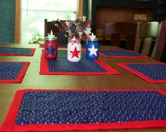 Peut inclure: Une table de salle à manger en bois avec des sets de table rouge et bleu à pois blancs. Trois bocaux en verre avec des bougies sont sur la table, décorés d'étoiles rouges, blanches et bleues.
