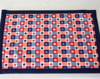 Peut inclure: Un set de table en tissu à carreaux rouge, blanc et bleu avec une bordure bleu marine. Le tissu a un motif d'étoiles blanches sur un fond à carreaux rouge, blanc et bleu.