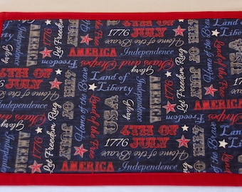 Peut inclure: Set de table en tissu rouge, blanc et bleu avec un motif répété des mots "America", "Independence", "4th of July", "1776", "Land of the Free", "Home of the Brave", et "Let Freedom Ring".