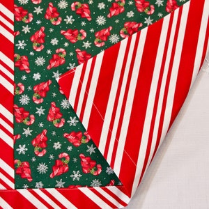 Puede incluir: Un camino de mesa navideño con un centro verde con bastones de caramelo y copos de nieve. El borde y el reverso tienen rayas rojas y blancas. Ideal para la decoración navideña.